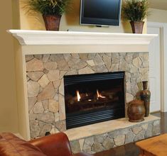 a living room with a stone fireplace and television on the mantle, two brown leather chairs in front of it