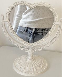 a white heart shaped mirror sitting on top of a table next to a woman's shirt