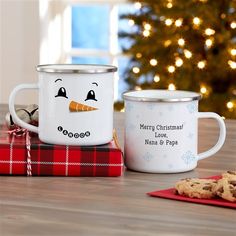 two white mugs sitting next to each other on top of a wooden table in front of a christmas tree