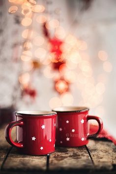 two red coffee mugs sitting on top of a wooden table next to a christmas tree