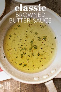 a white bowl filled with brown butter sauce on top of a wooden table next to plates and utensils