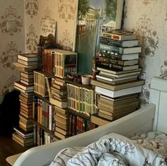 there is a bed with many books on top of it and a black cat in the corner