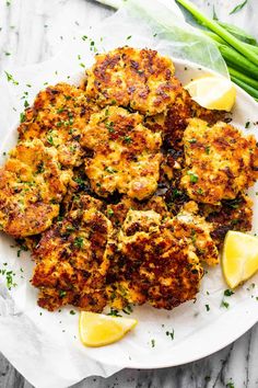 crab cakes on a plate with lemon wedges and chives next to it, ready to be eaten