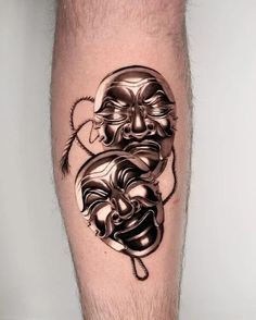 a man's leg with a tattoo on it that has two faces in the shape of masks