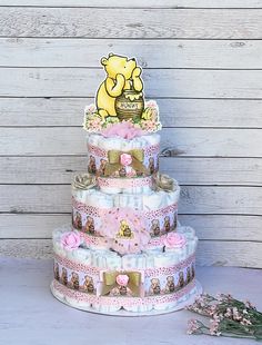 a three tiered winnie the pooh diaper cake with pink flowers on top