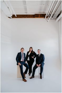 three people are posing for a photo in front of a white wall with exposed beams