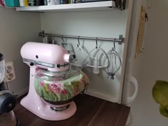 a pink mixer sitting on top of a wooden counter next to a shelf filled with kitchen utensils