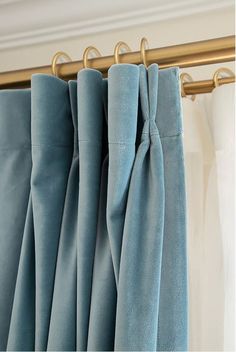 blue curtains hanging on a gold rod in front of a window with white drapes