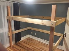 a loft bed frame in the corner of a room with wood flooring and curtains