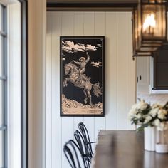 a dining room table and chairs in front of a painting on the wall above it