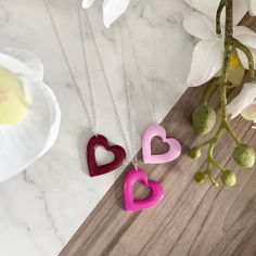 three heart shaped necklaces sitting on top of a table next to a vase with flowers