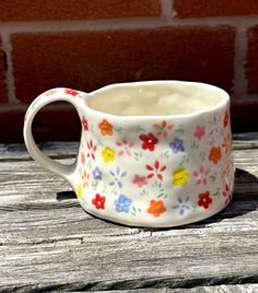 a flowered mug sitting on top of a wooden table next to a brick wall