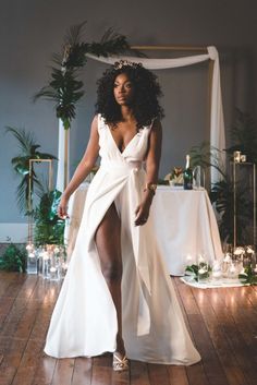 a woman in a white dress standing on a wooden floor with candles and greenery