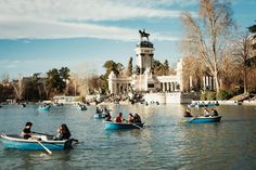 several people in small boats on the water near a statue and park with statues behind them