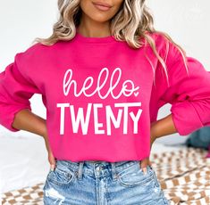 a woman wearing a pink sweatshirt with the words hello tweny printed on it