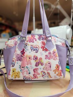 "Welcome to my Etsy listing for a custom purse, lovingly crafted with Generation 3 My Little Ponies fabric! This unique creation is a delightful fusion of nostalgia and style, perfect for any MLP enthusiast or lover of retro fashion. I've meticulously selected high-quality vinyl to complement the vibrant colors and whimsical designs of the Gen 3 fabric. The result is a durable and eye-catching purse that will withstand the test of time while turning heads wherever you go. To ensure comfort and c Custom Purses, Custom Handbags, Purse Handmade, Fabric Pictures, Novelty Bags, Top Handle Bags, Cute Bags, Custom Bags, Handbag Purse