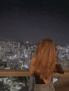 a woman standing on top of a tall building looking at the city lights in the distance