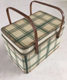 an old lunch box with leather handles and plaid pattern on the lid, sitting on a white surface