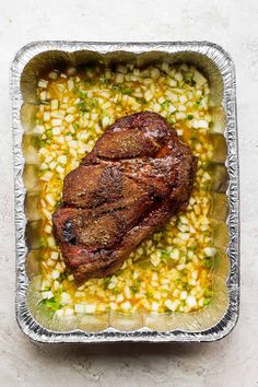 a piece of meat sitting on top of corn in a pan