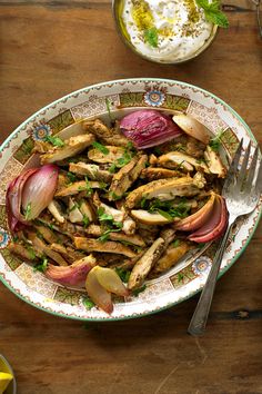 a plate filled with meat and vegetables on top of a wooden table next to a bowl of yogurt