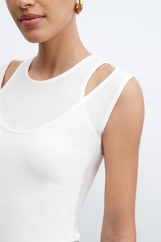 A sleeveless version of our much-loved Carson Top, Thea offers a strikingly unique neckline. Two layers of sheer, high-stretch European jersey combine with cutouts to create the look of a halter neckline layered with a classic round neck silhouette. With a sleek fit and edgy visual interest, Thea's an original alternative to your traditional tank that's day or night-ready.[SPLIT] Sam, in black and in spring green, is 5'8" (173 cm) tall, wearing size XS. Astrid, in off white and in raspberry, is Knit Sleeveless Sweater, Layered T-shirt, Sleeveless Fitted Halter Top For Summer, Fitted Top With Cutaway Shoulders For Spring, Stretch Cutout Halter Top For Summer, Spring Fitted Tank Top With Cutouts, Chic High Neck Tank Top For Layering, Fitted Sleeveless Top With Cutout Back, Stretch Scoop Neck Halter Top For Summer