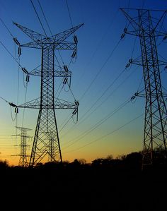 the sun is setting behind power lines and telephone poles in the foreground, with trees to the side