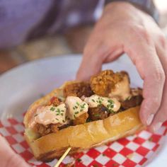 a person is holding a sandwich with meat and vegetables in it on a red and white checkered plate