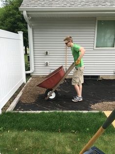 a man is pushing a wheelbarrow in the yard with his hand on it