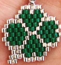 a green and white beaded shamrock pendant on a person's hand in front of the camera