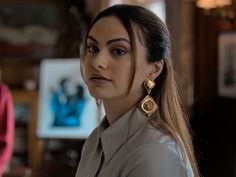 a woman with long hair wearing large gold earrings and a gray shirt is looking at the camera