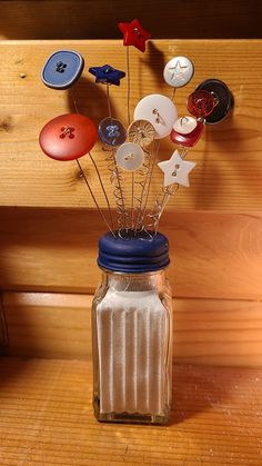 a mason jar filled with buttons and pins on top of a wooden shelf next to a wall