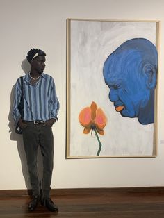 a man standing in front of a painting with a blue head and flower on it