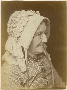 an old woman wearing a bonnet and holding a pipe in her mouth, looking off to the side