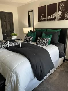 a bed with black and white sheets, green pillows and pictures on the wall above it