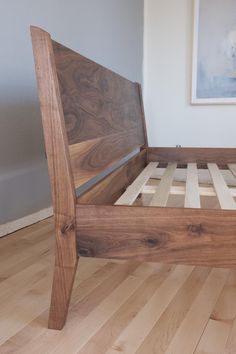 a wooden bed frame sitting on top of a hard wood floor next to a painting