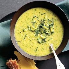 a bowl of broccoli and cheese soup next to a piece of bread