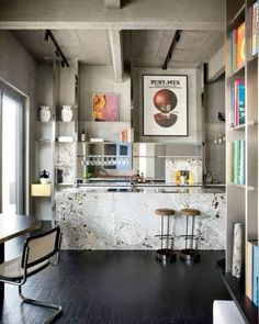 an industrial style kitchen with black floors and white marble counter tops, along with bookshelves