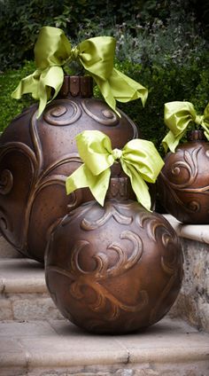 three brown vases with green bows on them are sitting on the steps in front of some bushes