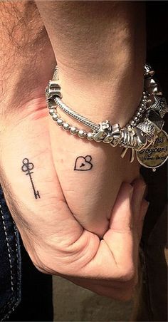 two people holding hands with tattoos on their fingers and one has a key to the heart