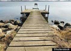 a wooden dock sitting on the side of a lake next to some rocks and grass