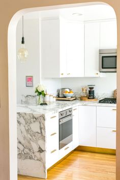 a kitchen with white cabinets and marble counter tops in an archway leading to the dining room