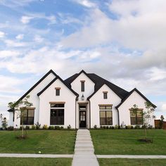 a white house sitting on top of a lush green field under a blue cloudy sky