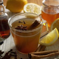 a cup filled with liquid next to some lemons and cinnamon on top of a table