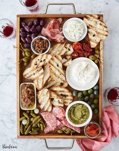 a platter filled with meats, cheese and crackers next to glasses of wine