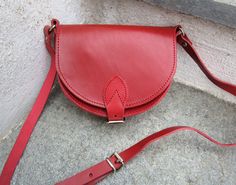 Saddle bag made from real cowhide leather in red.  Handmade in Greece. This small bag has two inner compartments with a zippered pocket under the flap and features an adjustable leather strap and buckle closure. Stored and remained unused since it was made this purse is in excellent condition free from wear. Suitable for essential items such as a wallet, lipstick and keys but may not fit most smart phones. Please see dimensions below. HEIGHT: 12cm (4.7 inches) WIDTH: 15cm (5.9 inches)  DEPTH: 5c Red Leather Saddle Bag With Adjustable Strap, Red Leather-lined Crossbody Shoulder Bag, Red Leather Crossbody Shoulder Bag, Red Leather Saddle Bag Shaped As Satchel, Red Leather Lined Satchel Shoulder Bag, Red Leather Saddle Bag In Satchel Shape, Red Leather Satchel Saddle Bag, Everyday Red Leather Saddle Bag, Red Leather Saddle Bag For Everyday