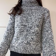 a woman wearing a black and white turtle neck sweater with long sleeves is standing in front of a wall