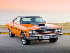 an orange and black muscle car parked on the side of the road next to the ocean