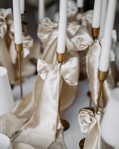 some white candles with bows on them are lined up in the middle of a table