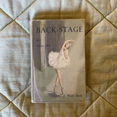 the back - stage book is laying on a quilted bed cover with a ballerina dancer in white