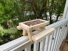 a bird feeder sitting on top of a wooden rail next to a white fence with trees in the background